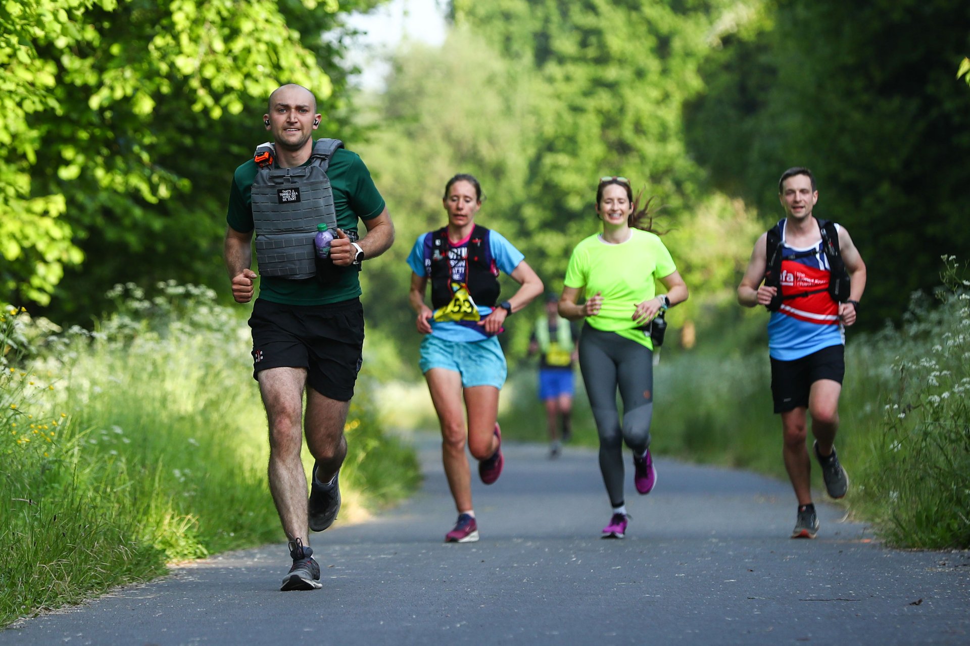 Runners participating in the Run2Paris relay from London to Paris, running through a lush green forest pathway.