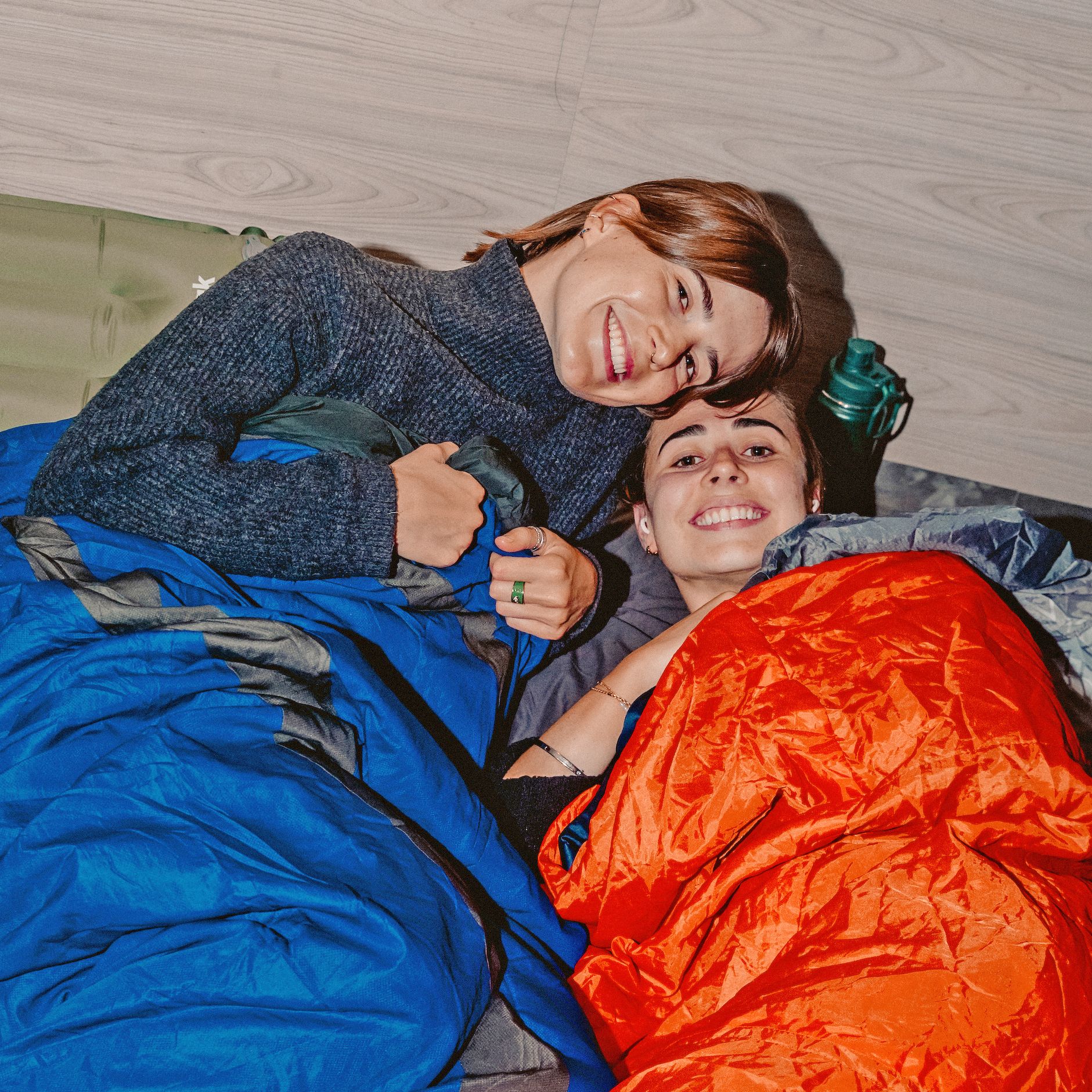 Smiling women lying inside sleeping bags, celebrating at the end of a relay run.