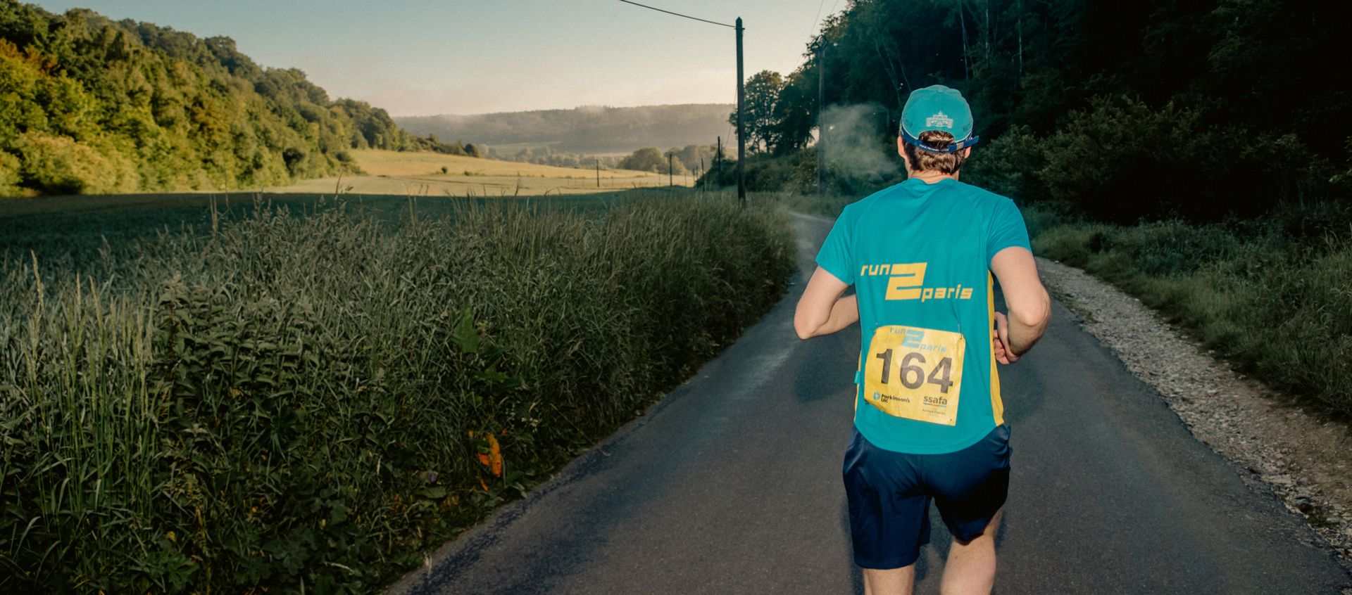 Running participant from behind on country road during Run2Paris relay event.
