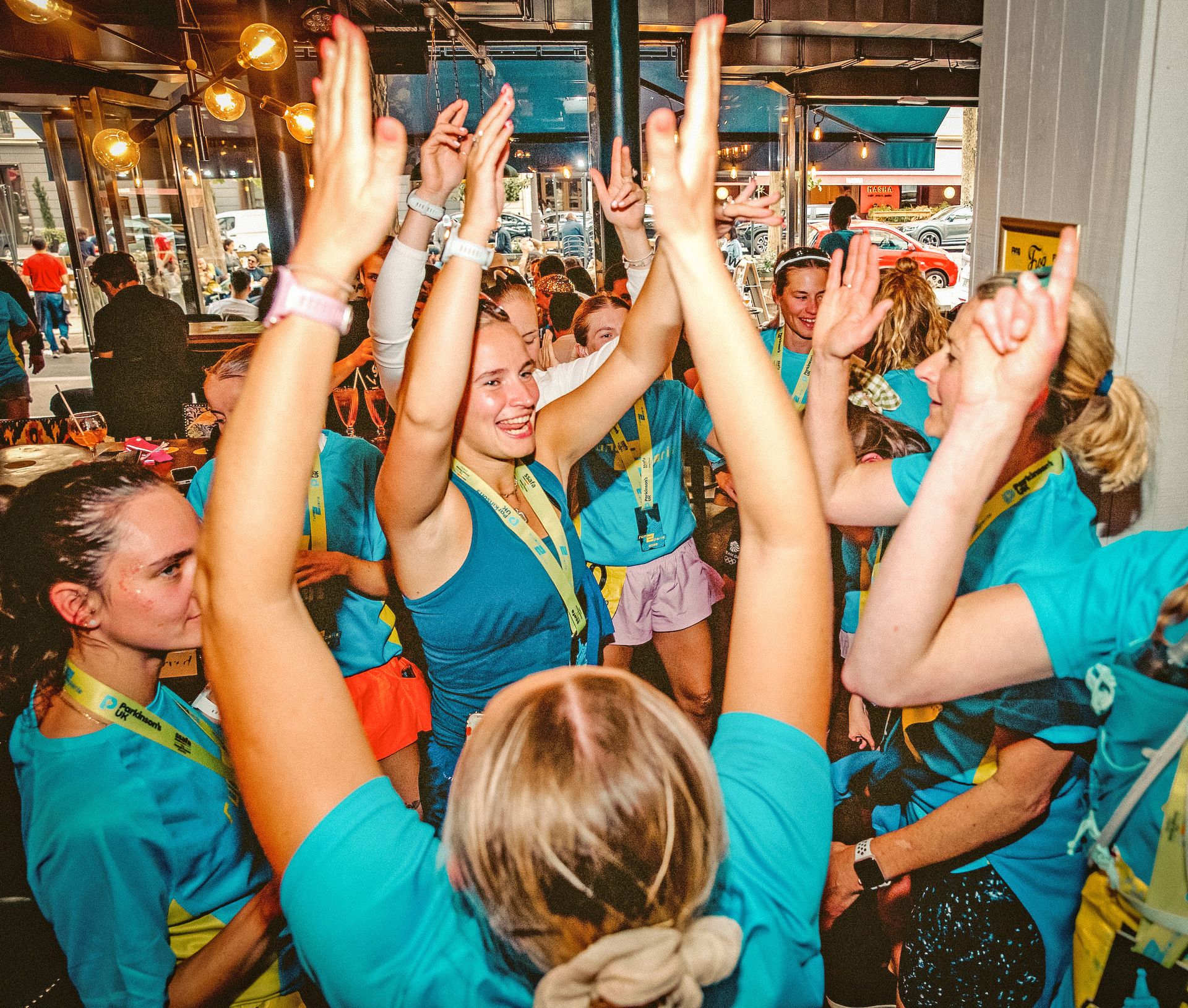 Cheering runners celebrating at an indoor event with medals in blue shirts.