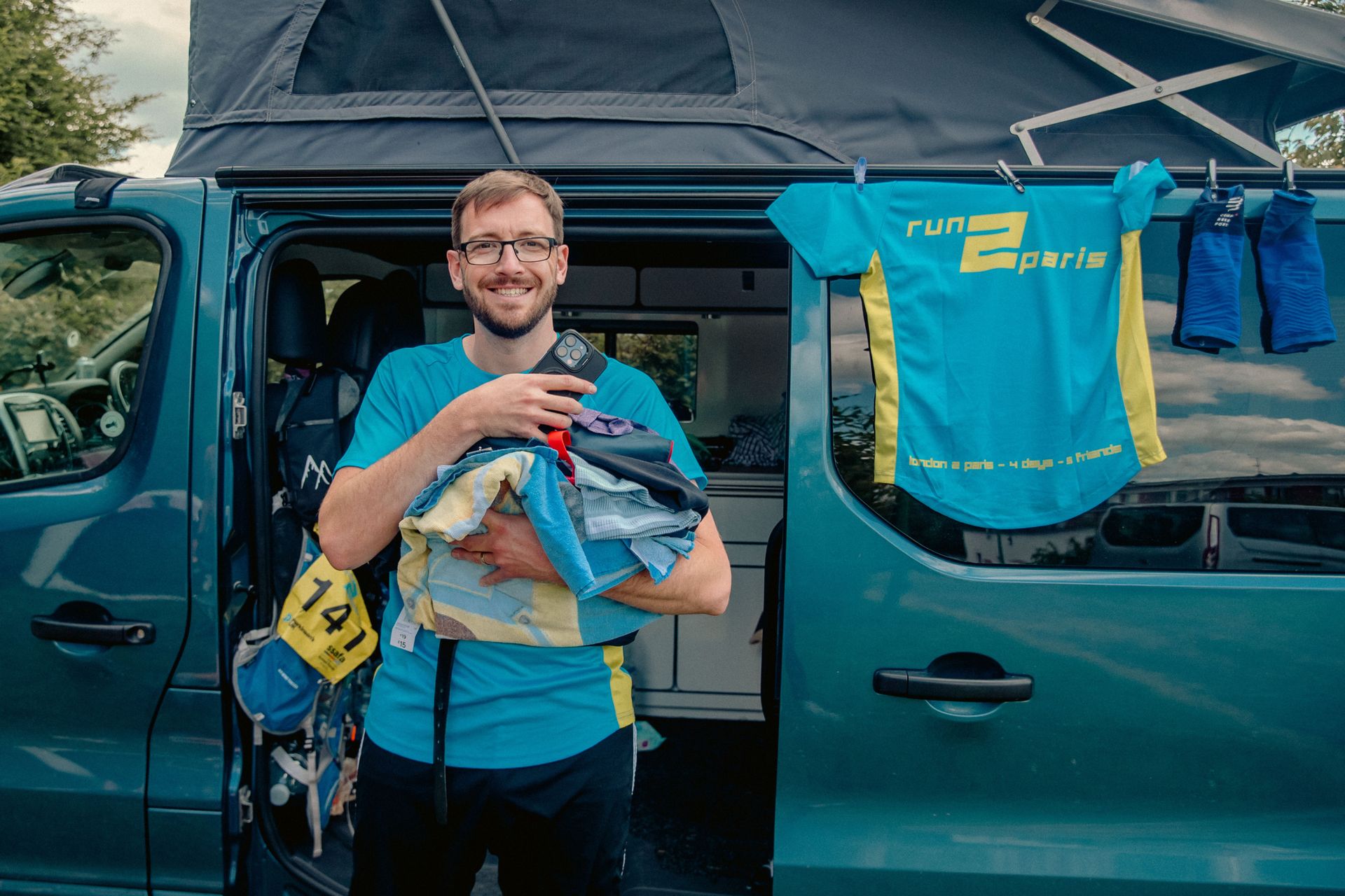Athlete with running gear and race bib beside a support vehicle for Run2Paris relay race.