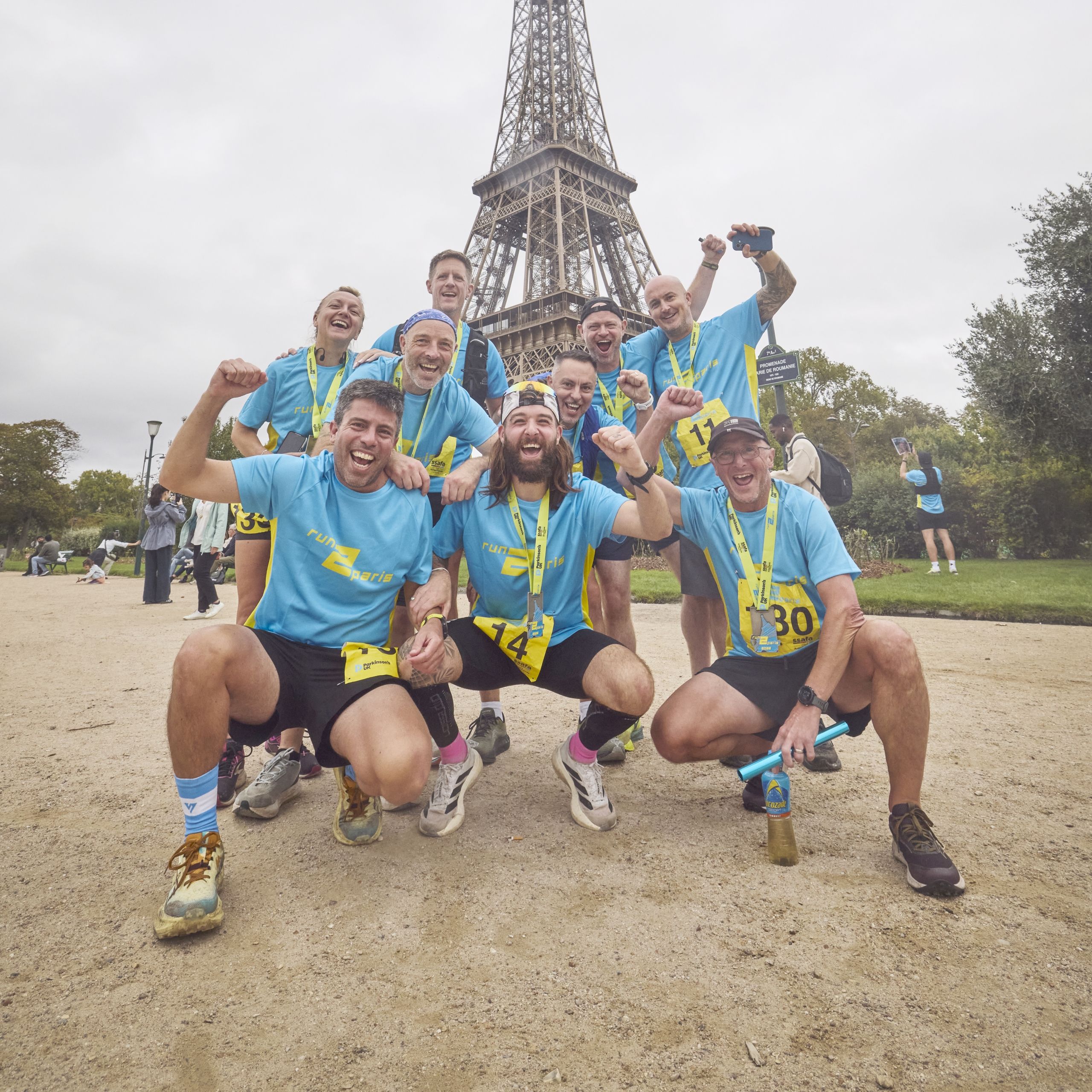 Teams celebrating after completing the Run2Paris relay from London to Paris, with the Eiffel Tower in the background.