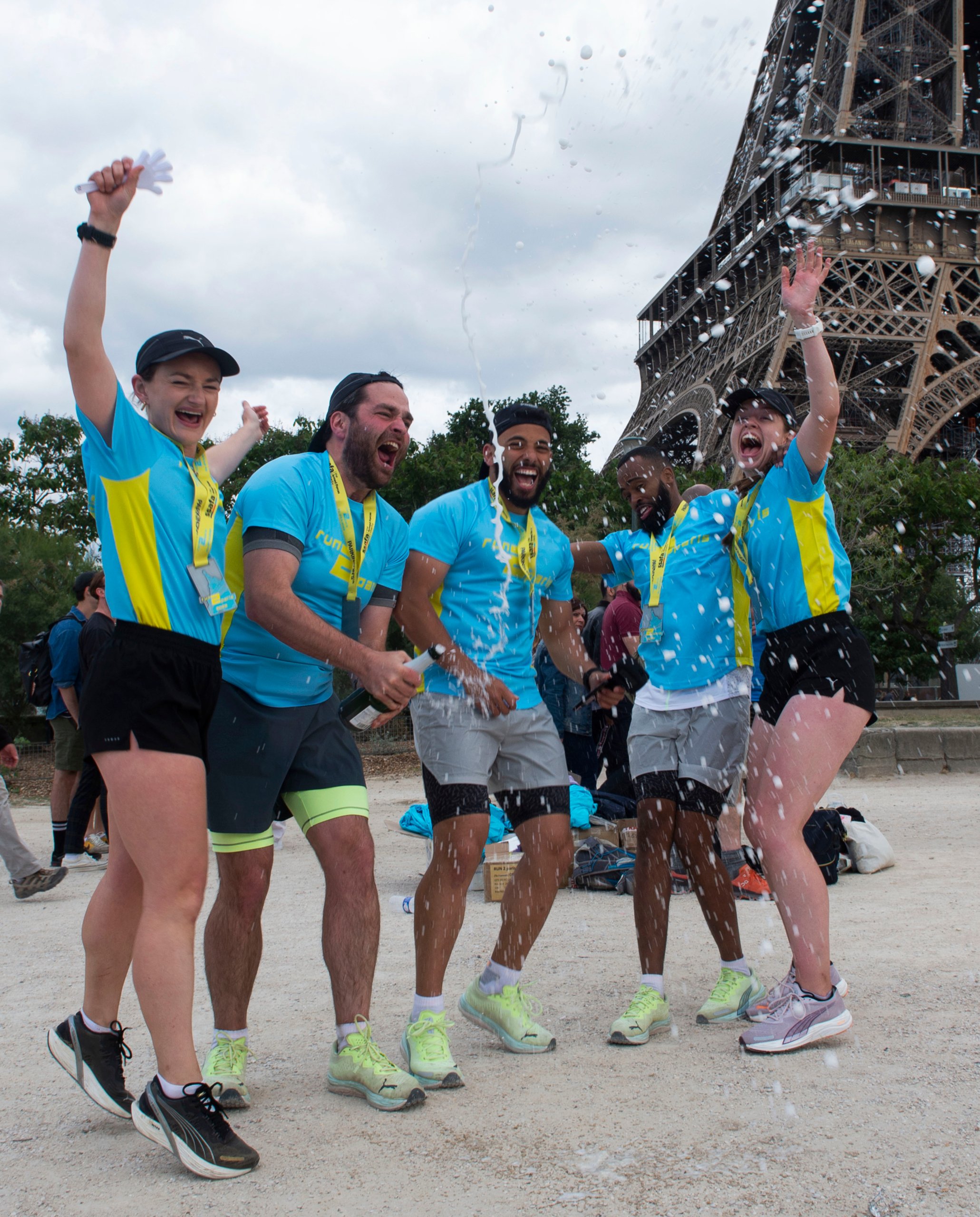 Cheerful runners celebrating with champagne in front of the Eiffel Tower during the Run2Paris relay event.