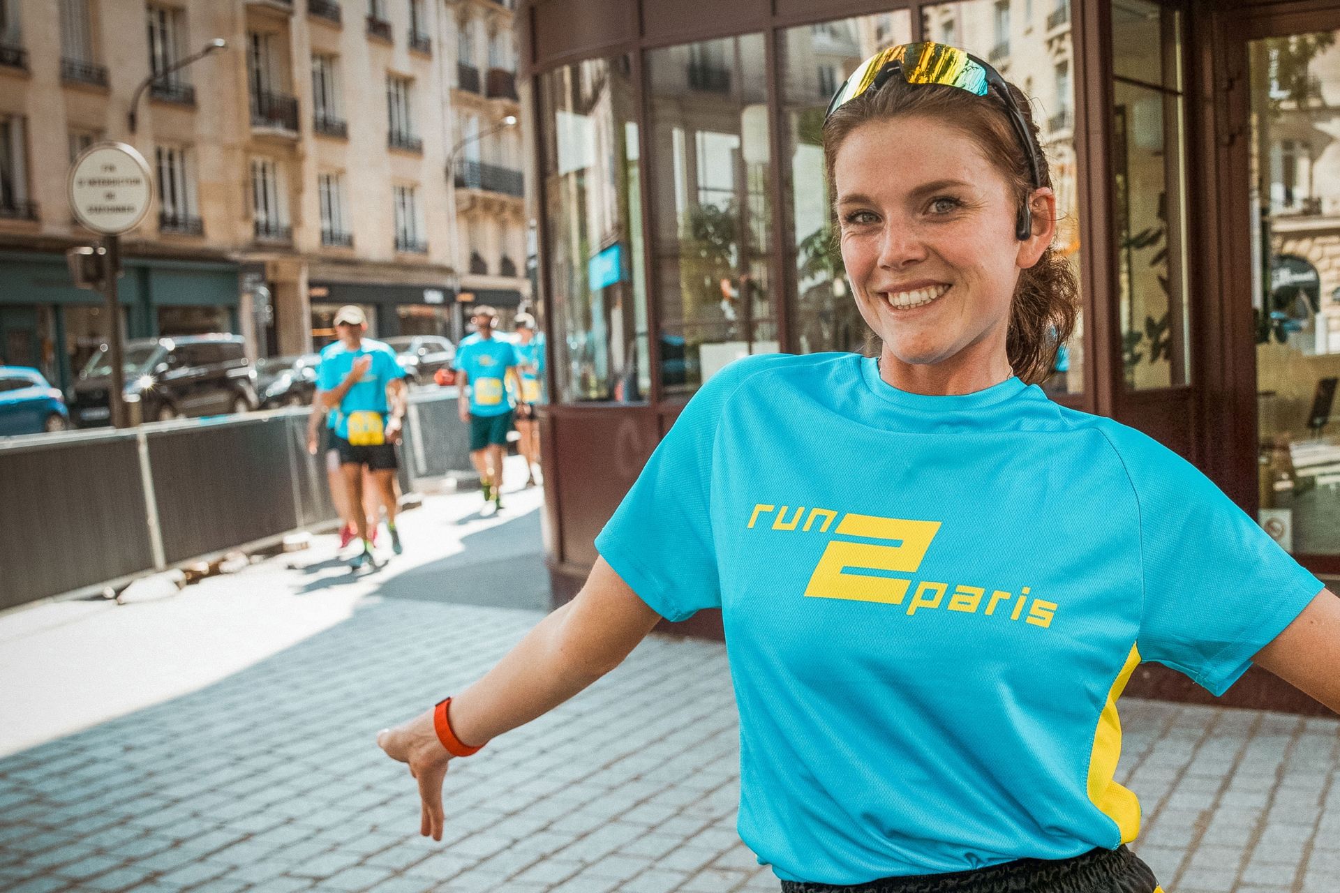 Bright female runner smiling wearing a blue Run2Paris T-shirt, post-race in Paris city centre.
